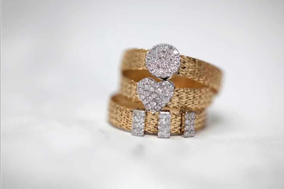 Gold woven ring with diamond circle, heart, and bar accents.