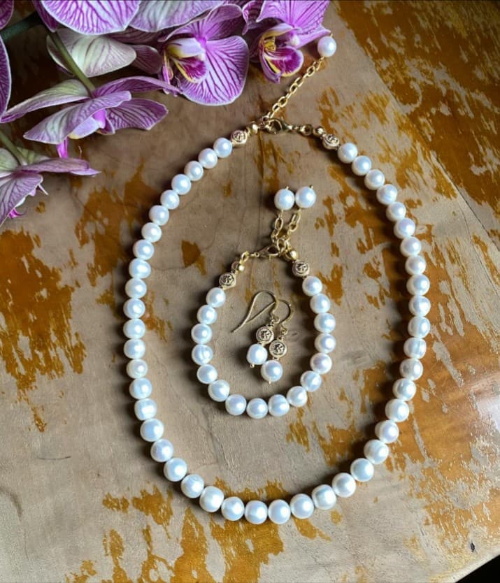 Pearl necklace, bracelet and earring jewelry set on a wooden surface.