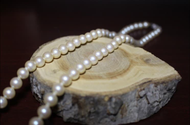 Elegant pearl necklace jewelry displayed on rustic wood slice.