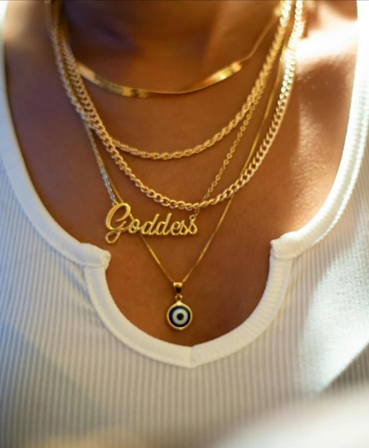 Gold layered necklaces: herringbone chain, rope chain, "Goddess" nameplate, evil eye pendant.